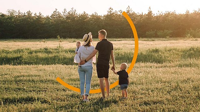Eine junge Familie steht auf einer Wiese. Die Eltern schauen sich an.