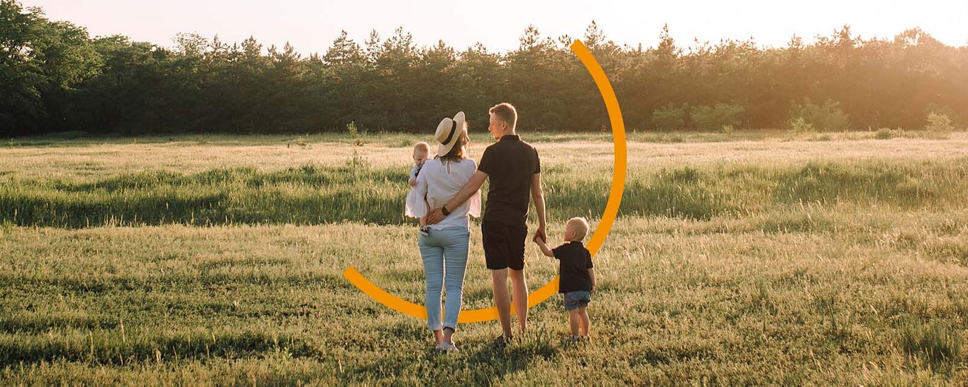 Eine junge Familie steht auf einer Wiese. Die Eltern schauen sich an.