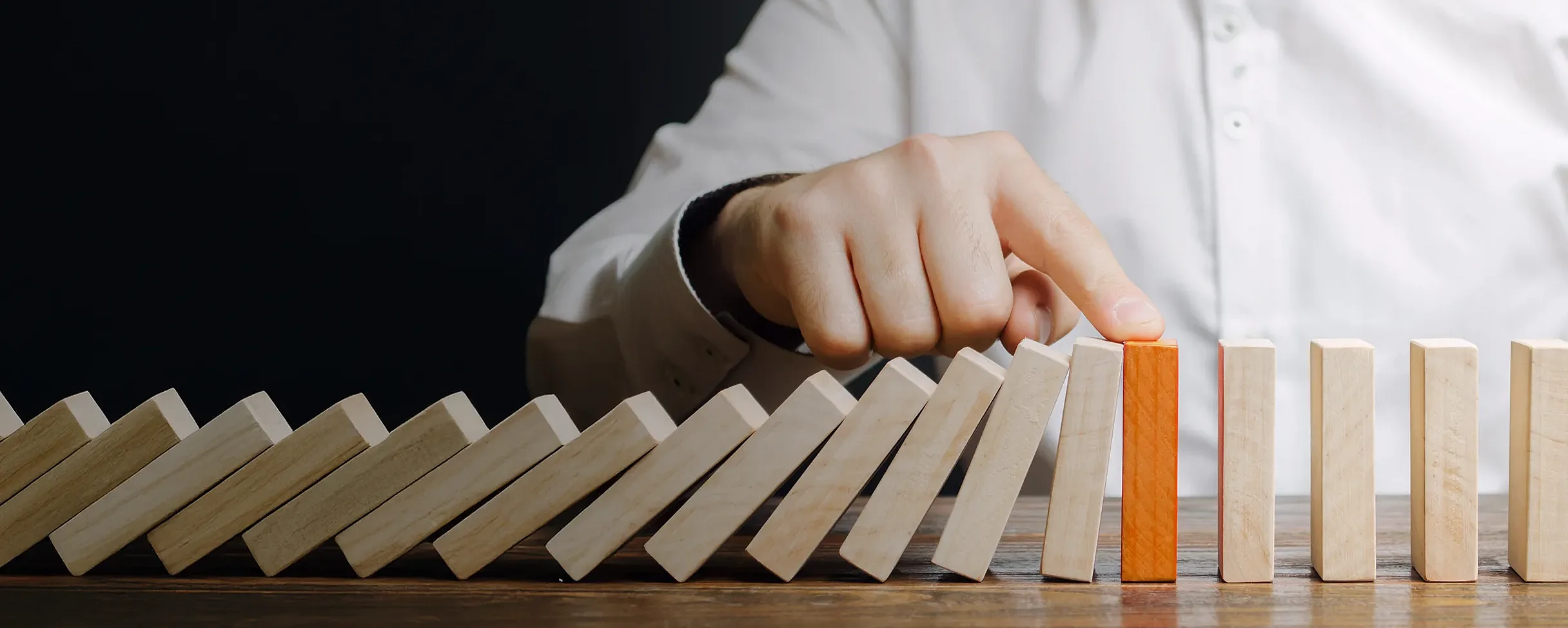 Eine Hand hindert eine Reihe Domino-Steine am umfallen, indem sie den Finger auf einen Stein legt