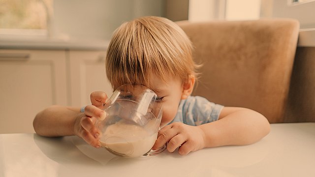 Ein kleiner Junge trinkt aus einem Glas Pflanzendrink.