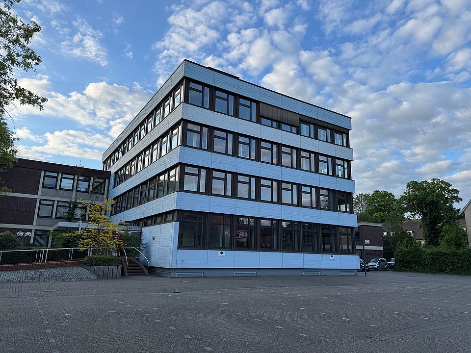 Standort Oldenburg Ein modernes vierstöckiges Bürogebäude mit großen Fenstern vor einem teilweise bewölkten Himmel.