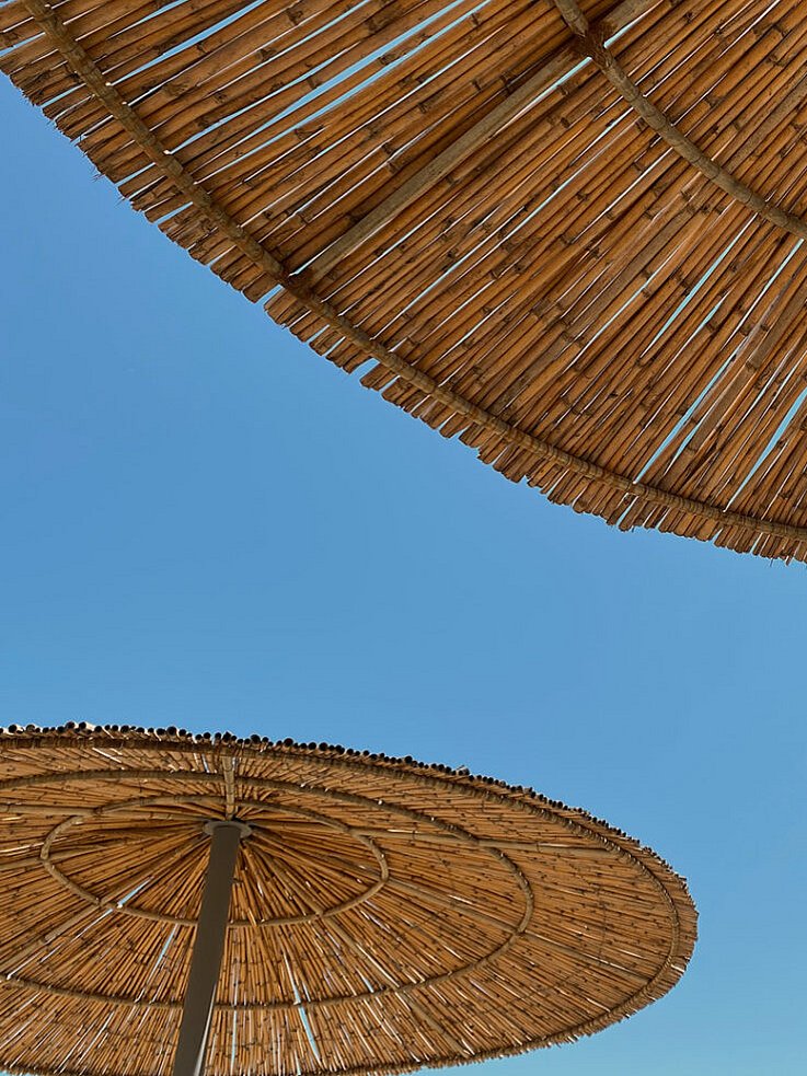 Zwei große, runde Strandschirme aus Stroh überlappen sich leicht unter einem strahlend blauen Himmel, von unten betrachtet.