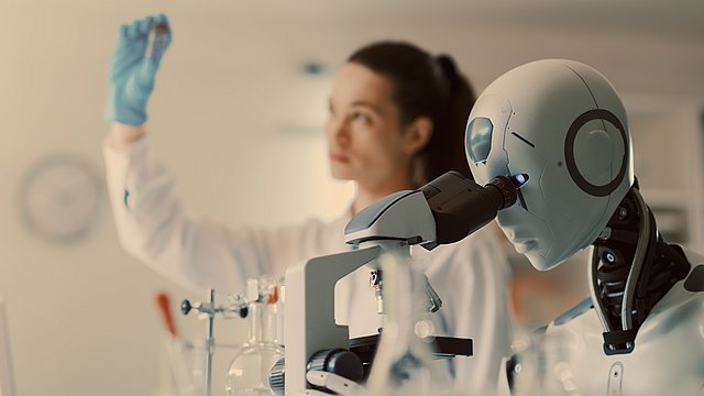 Ein Roboter blickt durch ein Mikroskop, während ein Wissenschaftler im Hintergrund ein Reagenzglas hochhält – in einem Labor, das mit Glasgeräten und wissenschaftlichen Instrumenten ausgestattet ist.