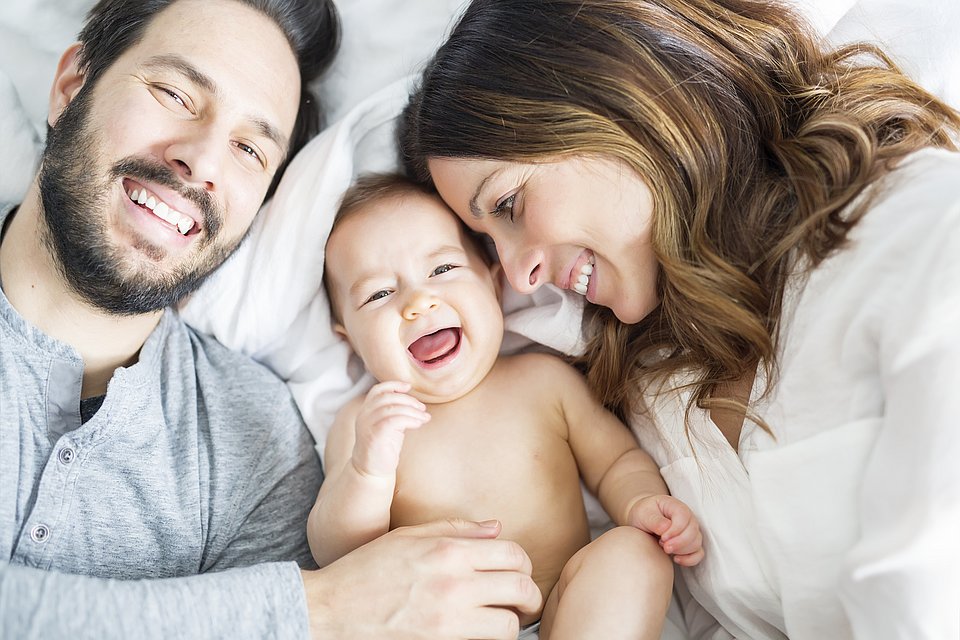 Eine lächelnde Mutter und ein lächelnder Vater liegen im Bett mit ihrem glücklichen Baby zwischen ihnen.