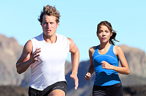 Mann und Frau beim Joggen im Freien an einem sonnigen Tag mit Bergen im Hintergrund.