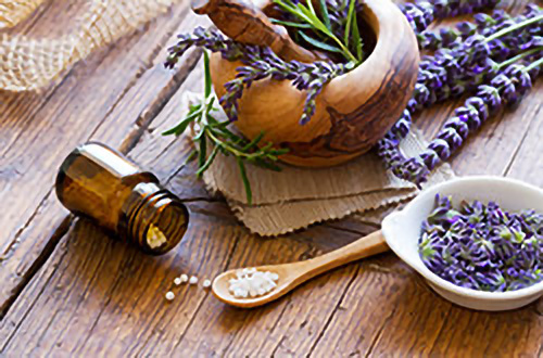 Braunglasflasche, Lavendelblüten, Holzlöffel mit weißen Pillen und eine Schale mit Lavendel auf einem rustikalen Tisch.