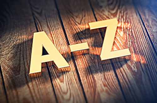 Goldene Buchstaben von A-Z auf einem Holzboden mit dramatischer Beleuchtung und Schatten.