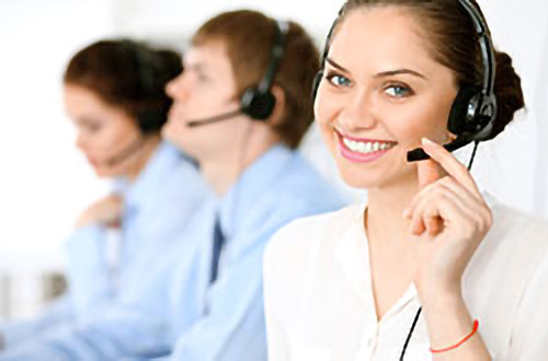Lächelnde Frau mit einem Headset in einem Callcenter, im Hintergrund arbeiten zwei Kollegen.