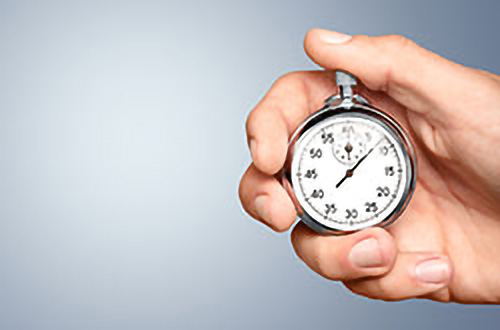 Eine Hand, die eine Stoppuhr vor einem einfarbigen Hintergrund hält.