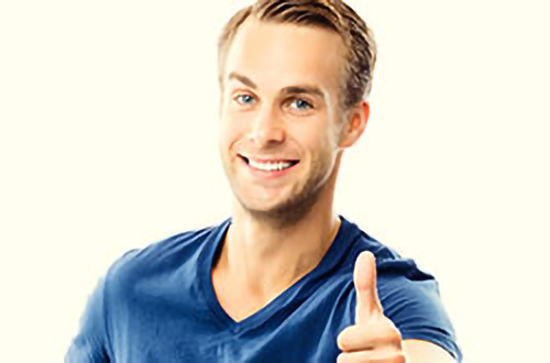 Lächelnder Mann in einem blauen T-Shirt, der vor einem hellen Hintergrund den Daumen nach oben streckt.