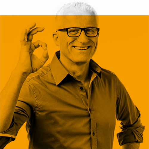 Lächelnder Mann mit Brille, der eine OK-Handgeste macht, stehend vor einem orangefarbenen Hintergrund.