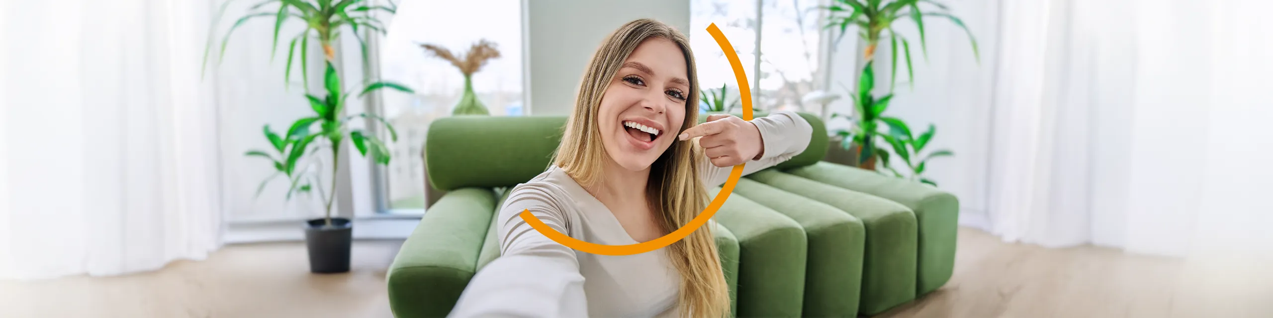 Eine blonde Frau lächelt in die Kamera und deutet auf Ihre Zähne.