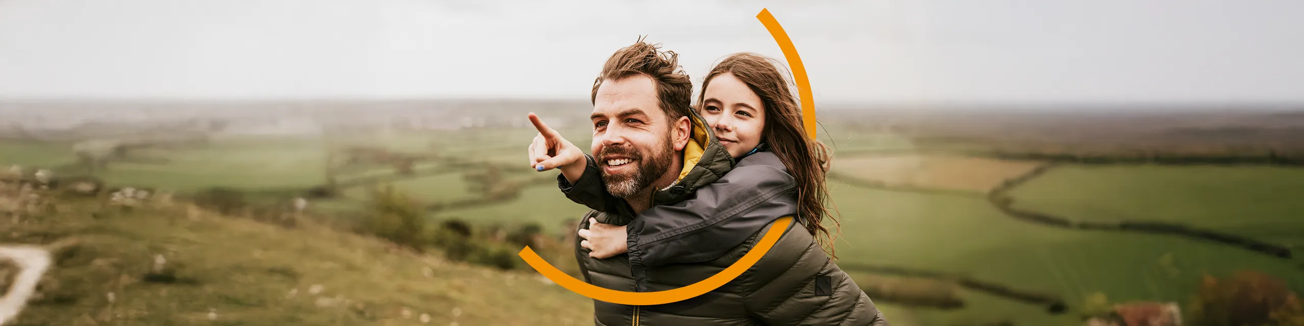 In einer grünen Landschaft trägt ein Mann seine Tochter auf dem Rücken, sie deutet in die Ferne.