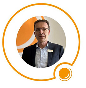 Ein Mann im Anzug und mit Brille posiert innerhalb einer orangefarbenen Kreisgrafik auf weißem Hintergrund.