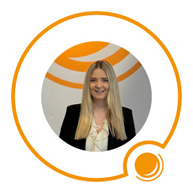 Lächelnde Frau mit langen blonden Haaren, die einen schwarzen Blazer trägt, vor einem orange-weißen Hintergrund.